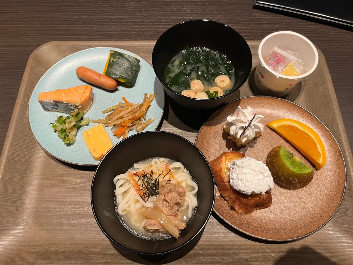 木質托盤上擺放烏冬、味噌湯、烤三文魚、水果與乳酪的日式早餐